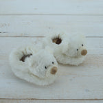 Pair of white plush bear slippers on a light wooden floor.