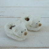 Pair of white plush bear slippers on a light wooden floor.