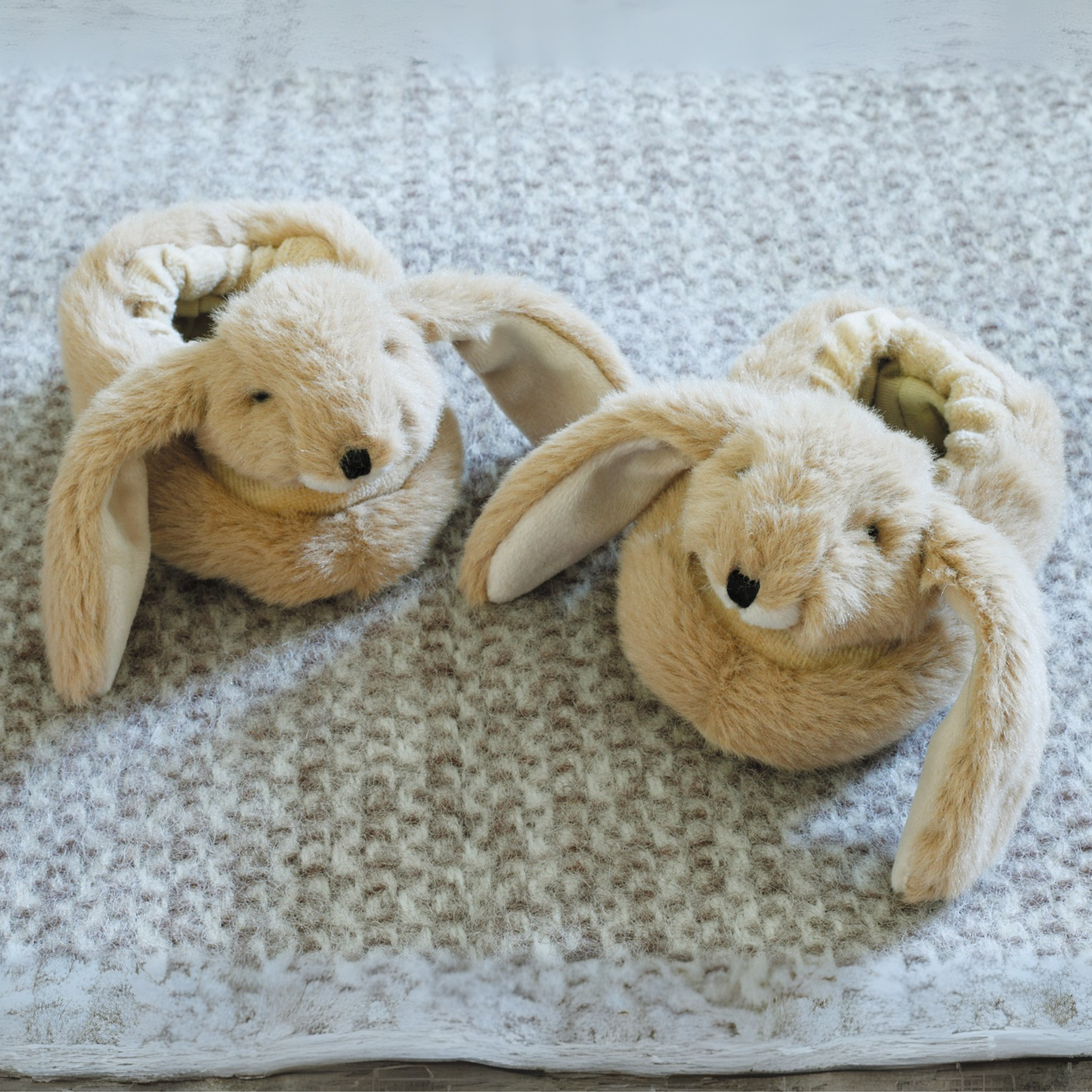 Pair of beige bunny slippers on a textured surface