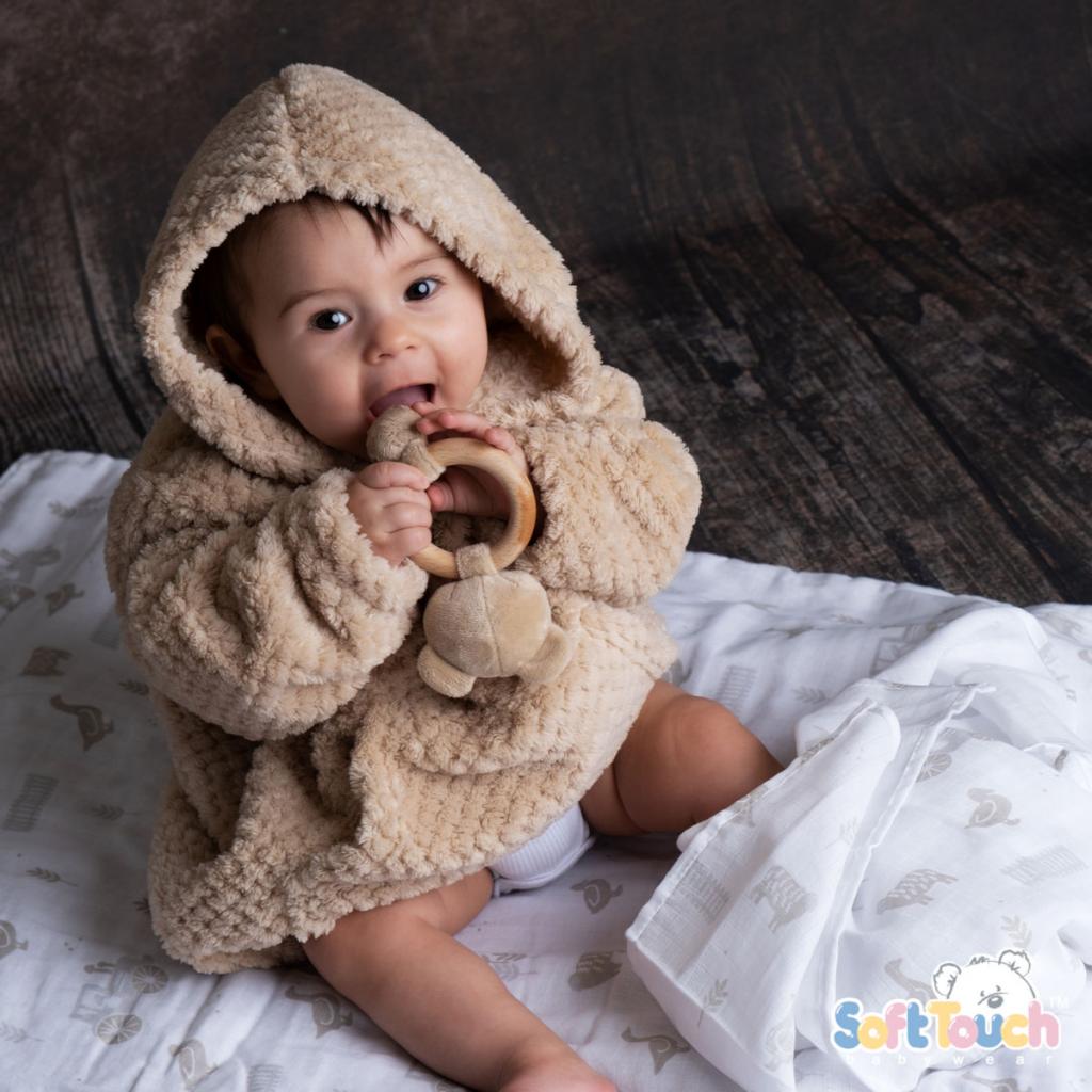 A baby wearing a beige hooded waffle texture jacket with a pocket, sitting on a blanket.