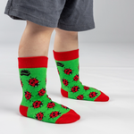 Green socks with red accents and ladybug pattern worn by a person on a white background