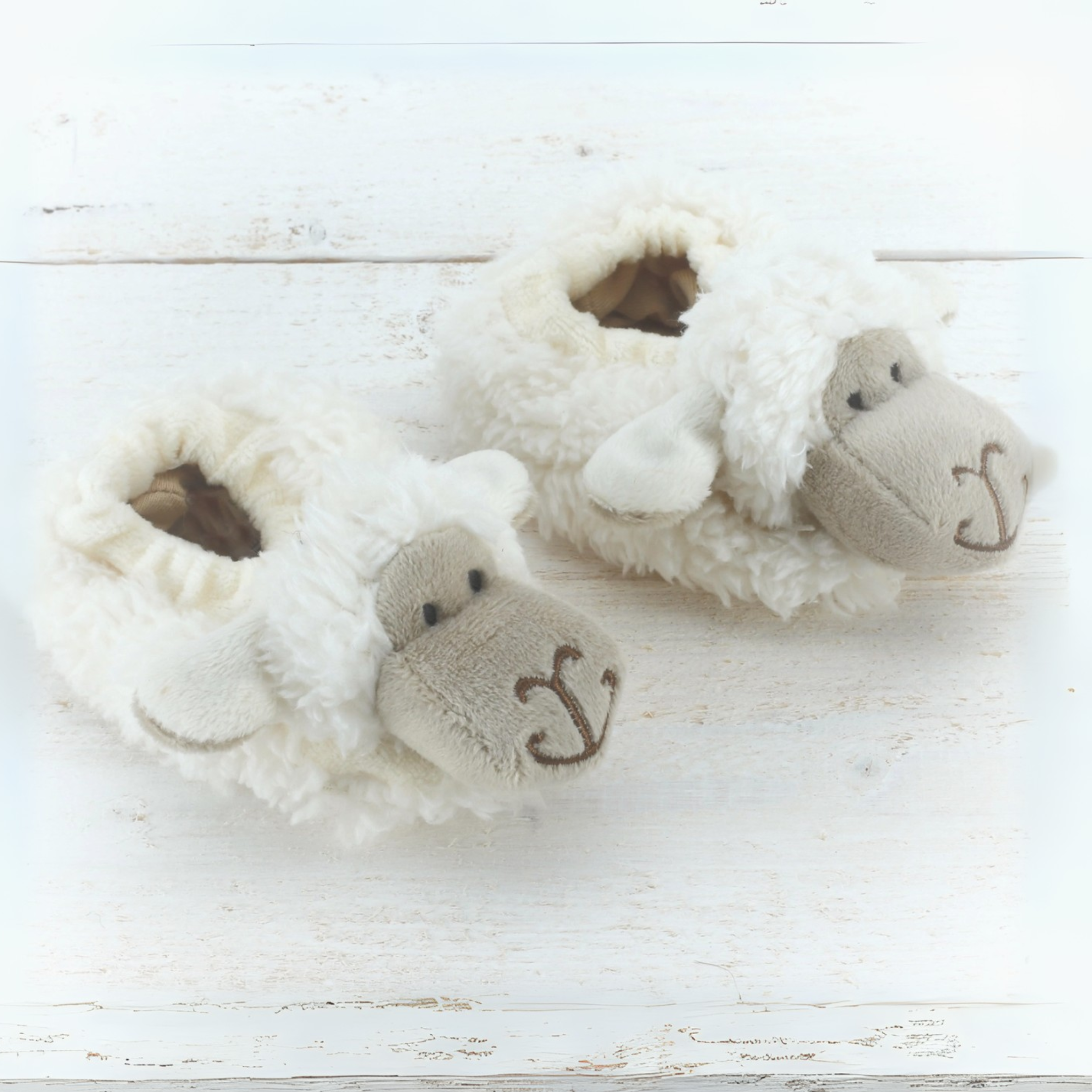 Pair of fluffy slippers with cartoon face design on a light wooden surface
